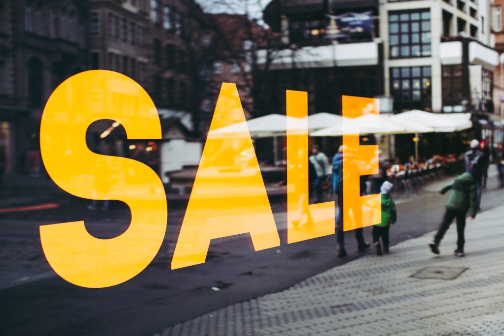 Bright yellow 'Sale' sign in a store window reflecting a busy street scene, attracting shoppers with discounts